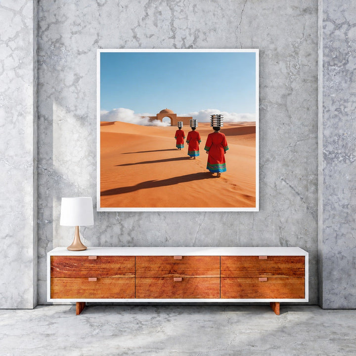 Wadi Home artwork: Three figures in red robes walk across desert dunes towards an archway, carrying items on their heads.