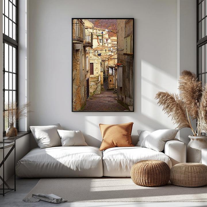 Wadi Home European village street scene wall art, sun-drenched alleyway with rustic buildings and balconies, warm earthy tones.