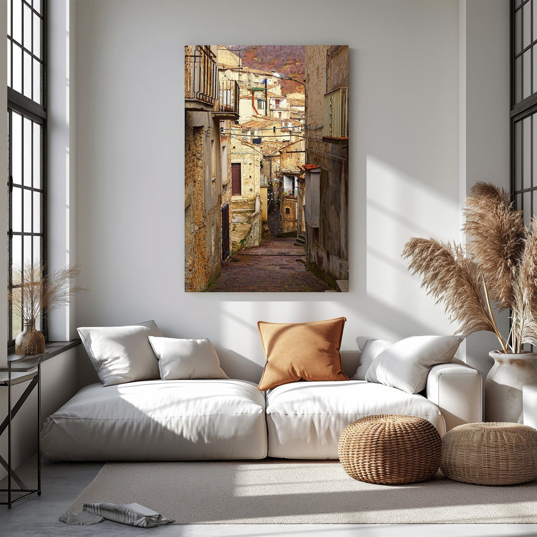 Wadi Home European village street scene wall art, sun-drenched alley with rustic buildings and balconies.