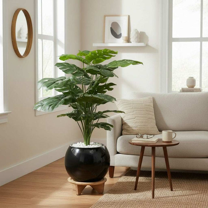 Wadi Home Large artificial Monstera plant with lush green split leaves in a glossy black pot with white stones.