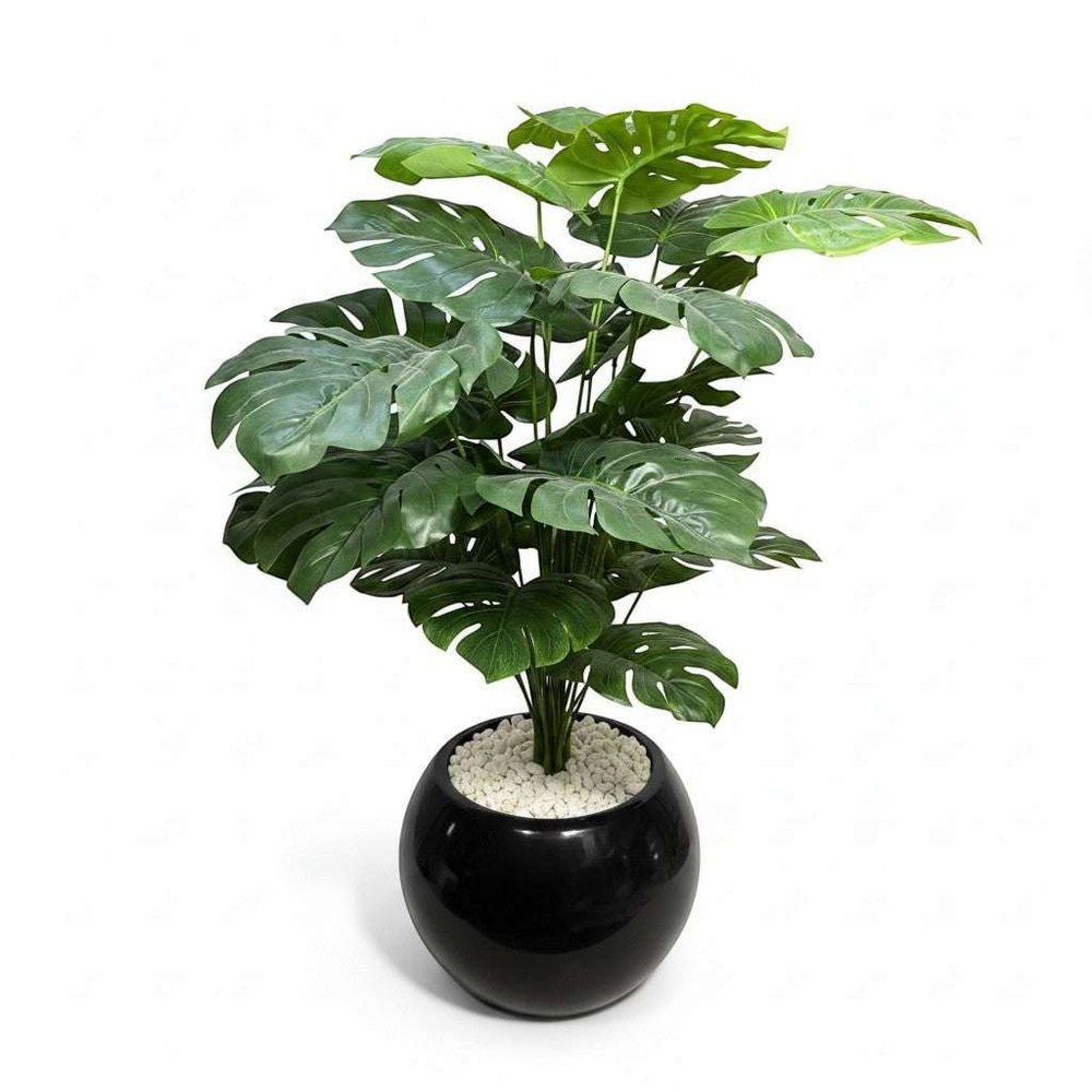 Wadi Home large artificial Monstera plant with lush green split leaves in a glossy black pot with white pebbles.