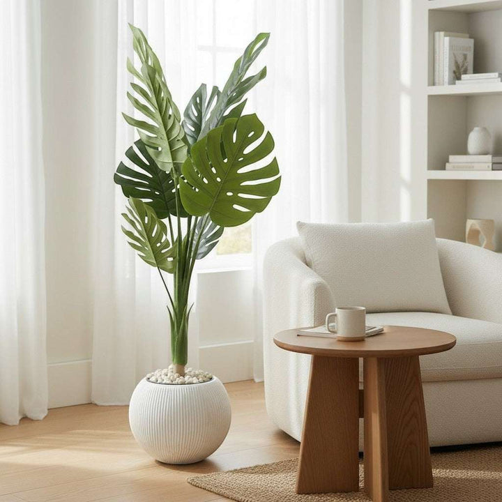 Wadi Home large faux monstera plant with split green leaves in a textured white pot, placed in a bright living room.