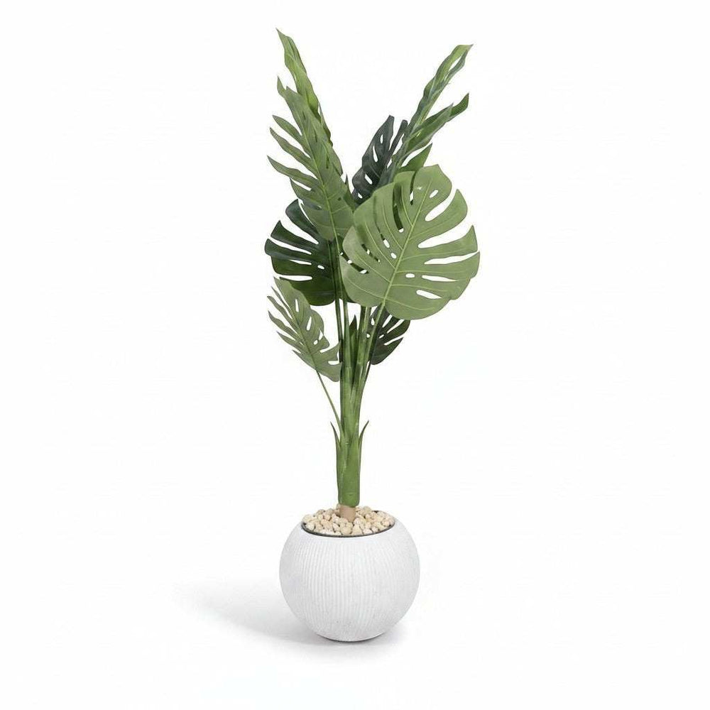 Wadi Home large faux monstera plant with split green leaves in a textured white spherical pot with pebbles.