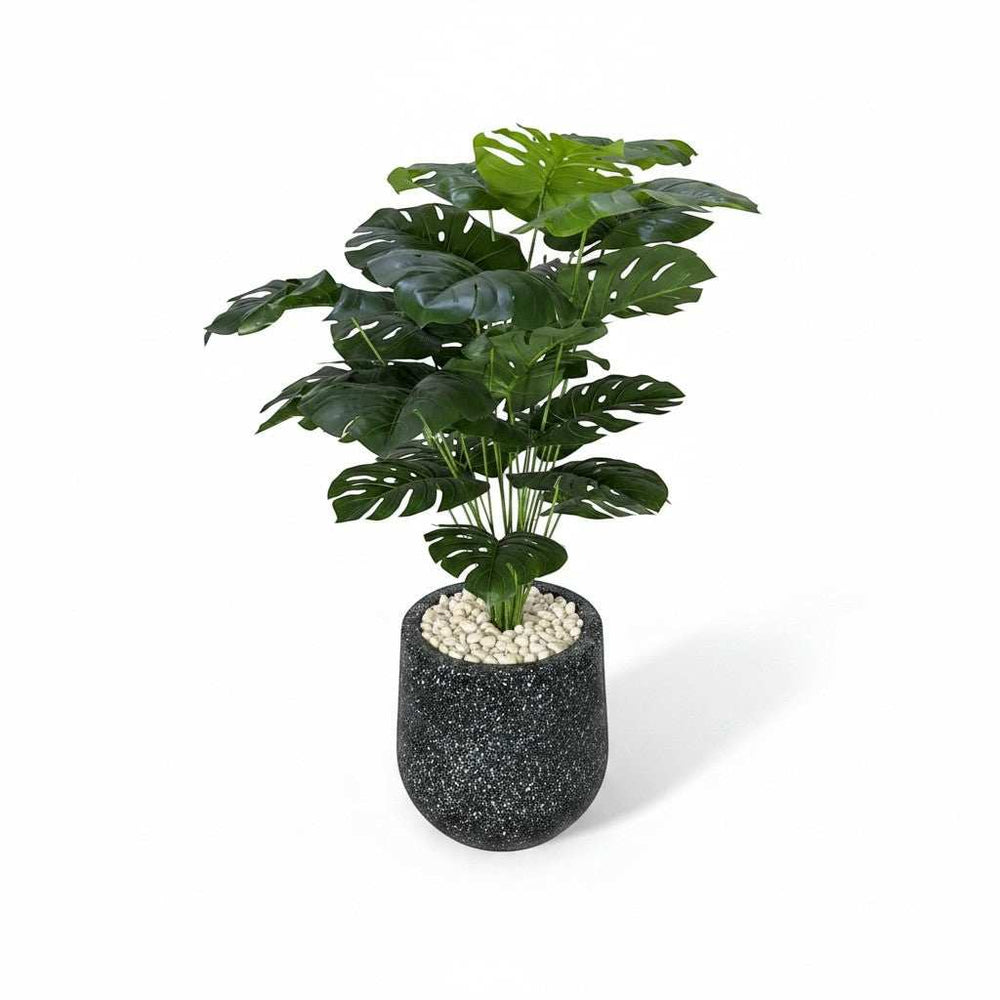 Wadi Home large artificial Monstera plant with split green leaves in a speckled black pot with white stones.