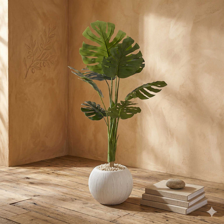 Wadi Home large artificial Monstera plant with deep green split leaves in a textured white pot with decorative stones.