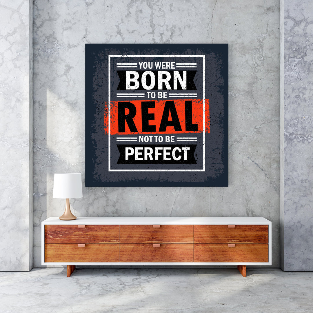 Wadi Home motivational wall art with bold white text on dark grey background: "You Were Born To Be Real Not To Be Perfect".