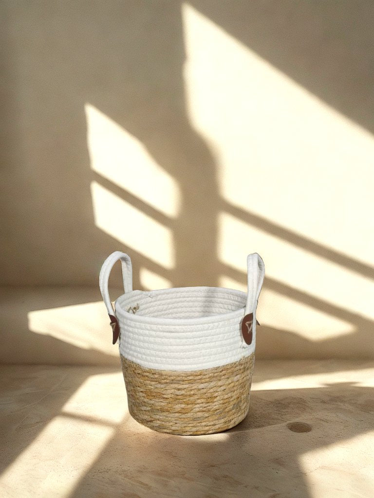 White and natural jute basket planter with loop handles and brown attachment tabs in a softly lit neutral interior.