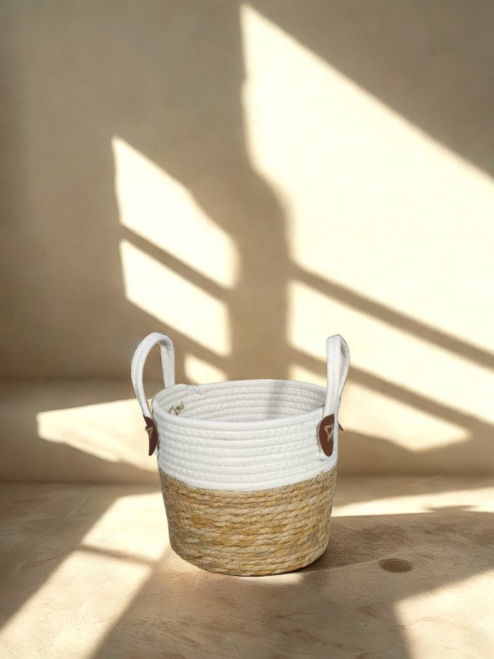 White and natural jute basket planter with loop handles and brown attachment tabs in a softly lit neutral interior.