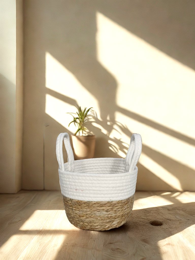 White and natural jute basket planter with white rope handles in a softly lit neutral interior.